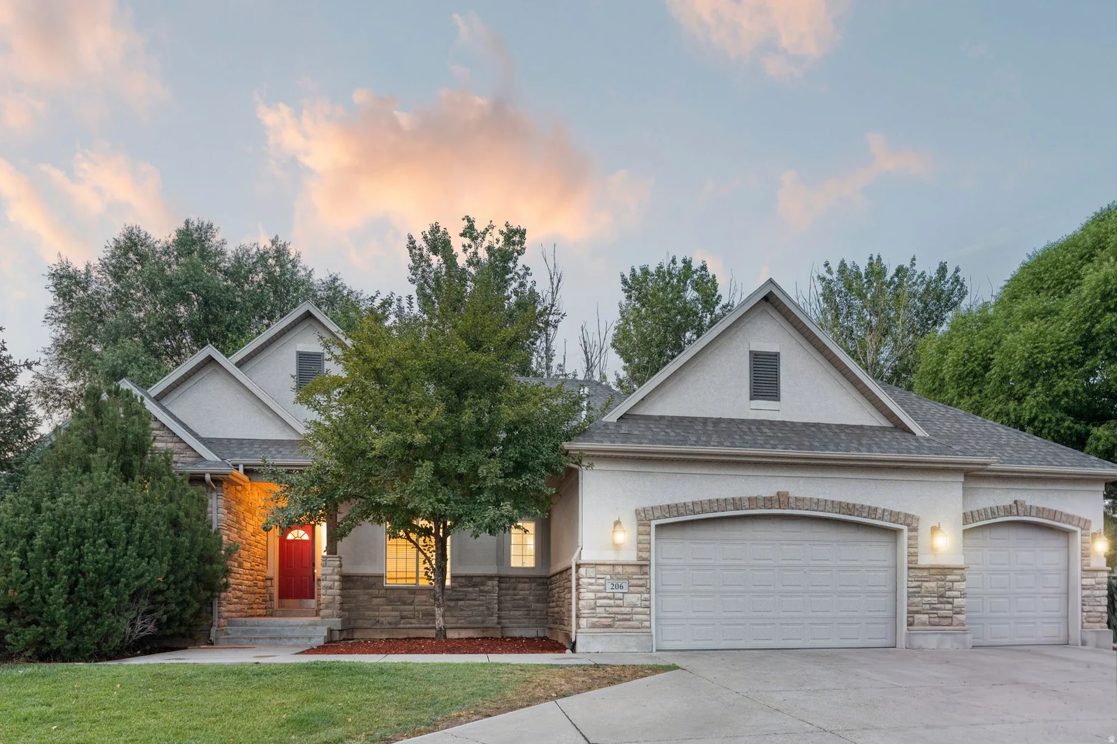 Exterior featuring a red entry door, stone and stucco facade, dual garage doors with arched brick accents, and a concrete driveway